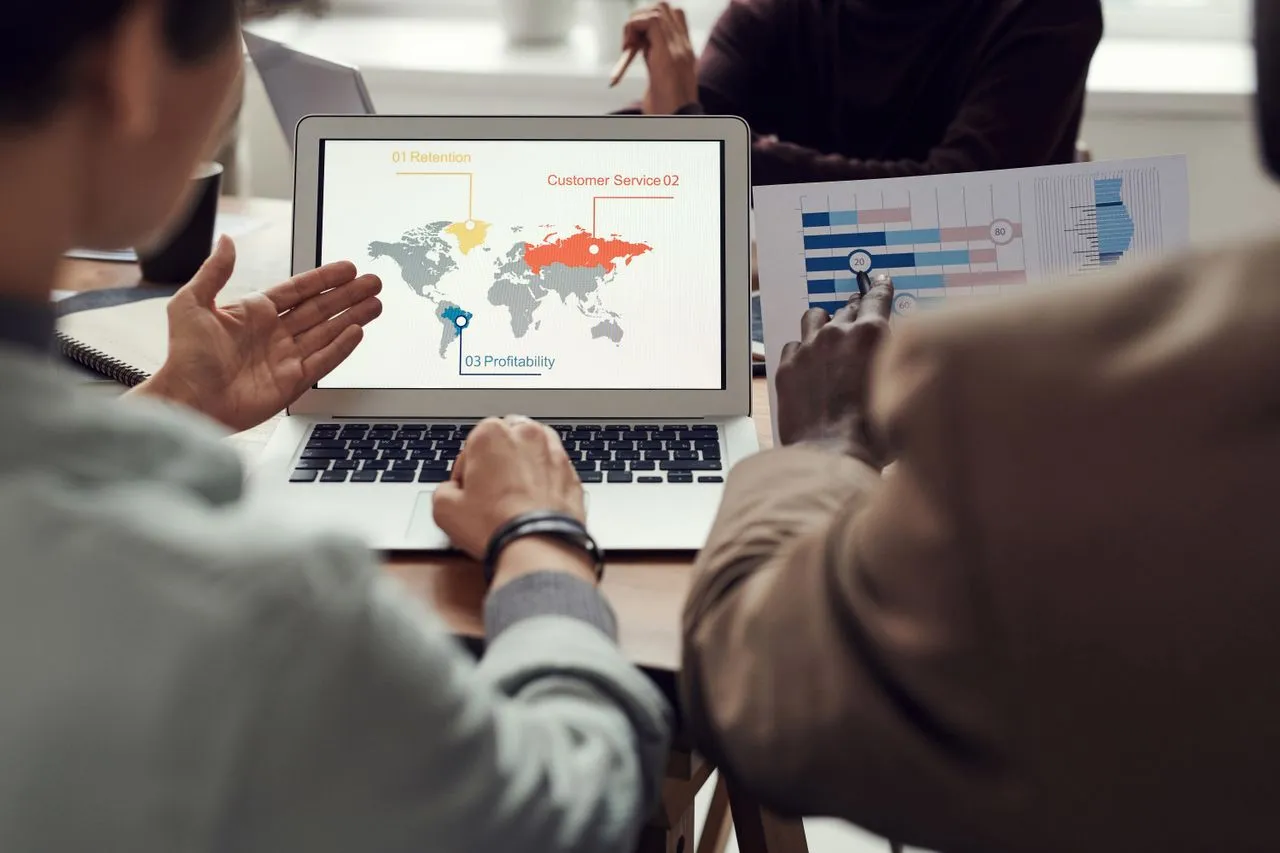 Two colleagues reviewing a world map dashboard on a laptop
