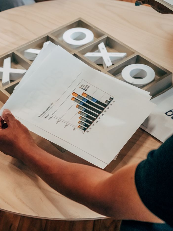 Crafting Captivating Headlines: Your awesome post title goes here Close-up of hand holding business analysis document with graphs, set on a wooden table indoors.